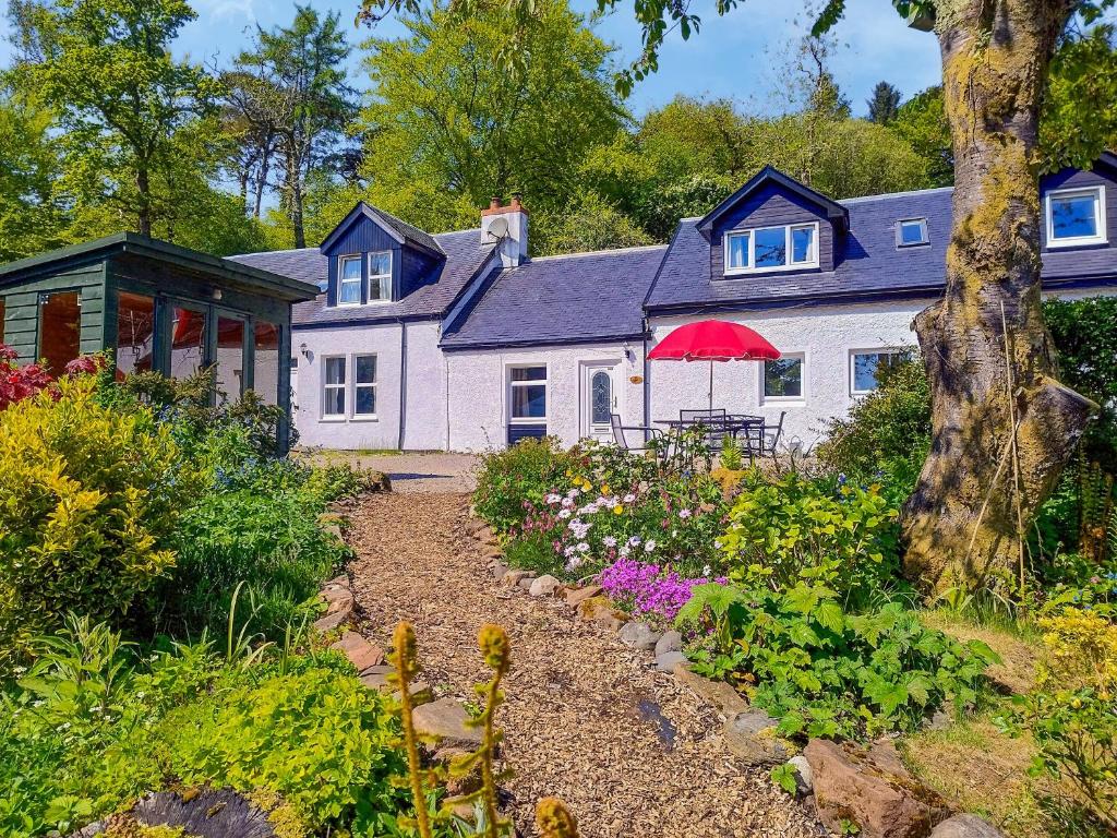 ein weißes Haus mit einem roten Sonnenschirm und einem Garten in der Unterkunft Old Steading in Brodick