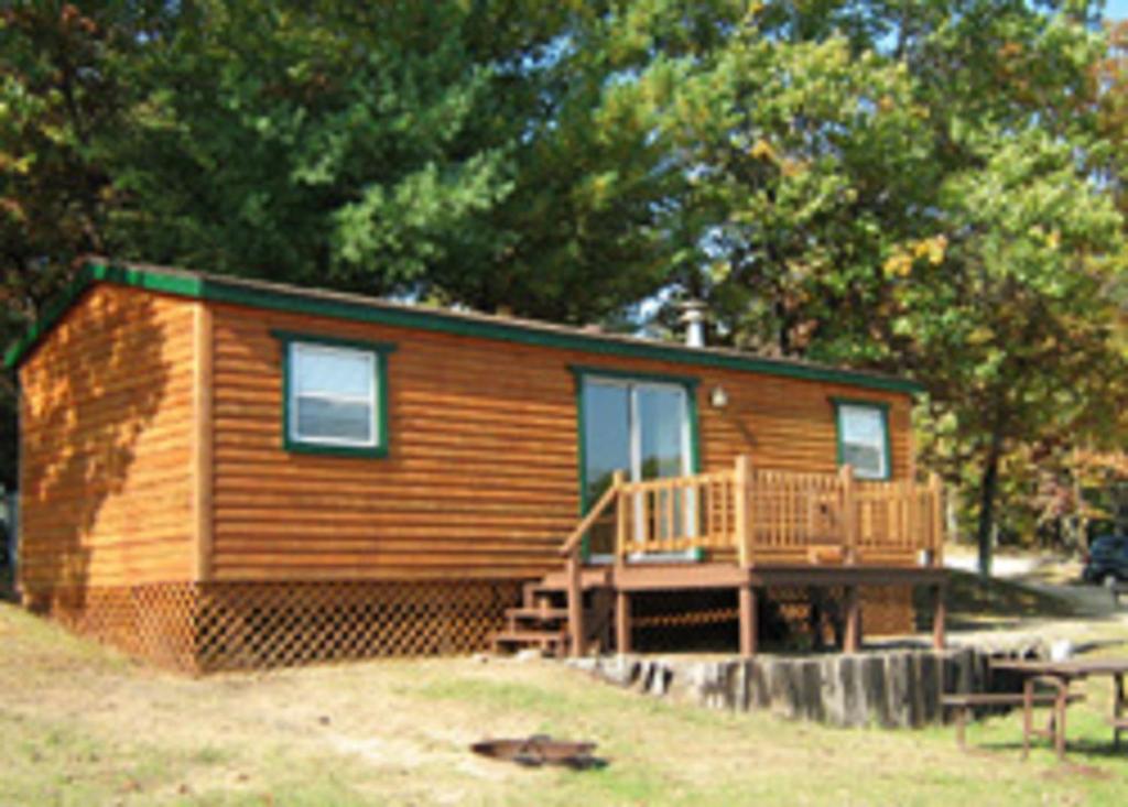 uma pequena cabana de madeira com um alpendre e um deque em Arrowhead Camping Resort Park Model 10 em Douglas Center