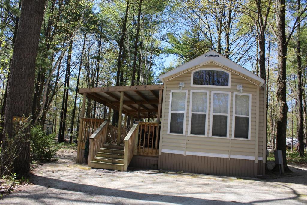 a tiny house in the woods with a porch at Tranquil Timbers Park Model 7 in Sturgeon Bay