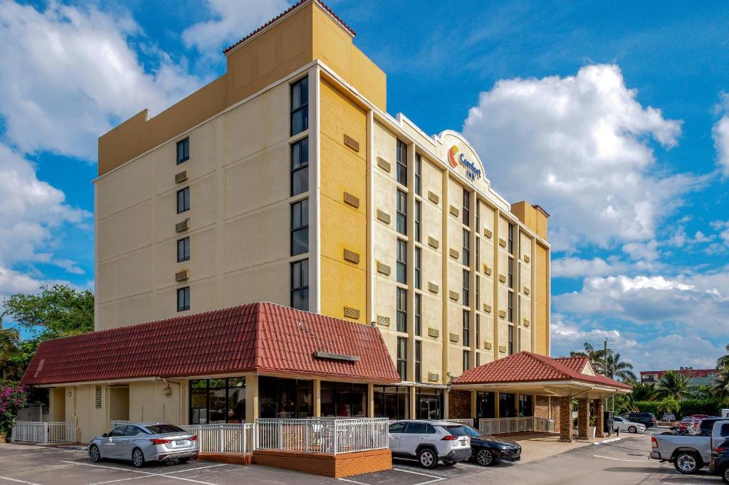 a large yellow building with cars parked in a parking lot at Comfort Inn Oceanside Deerfield Beach in Deerfield Beach