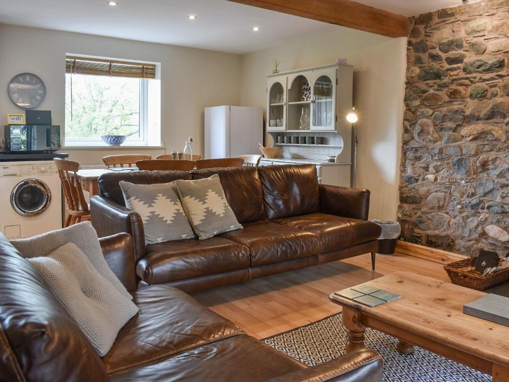 a living room with a leather couch and a stone wall at 1, The Barns in Threlkeld