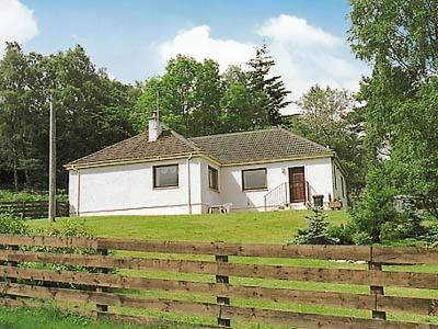 a white house in a field with a fence at Holly Cottage in Gorstan