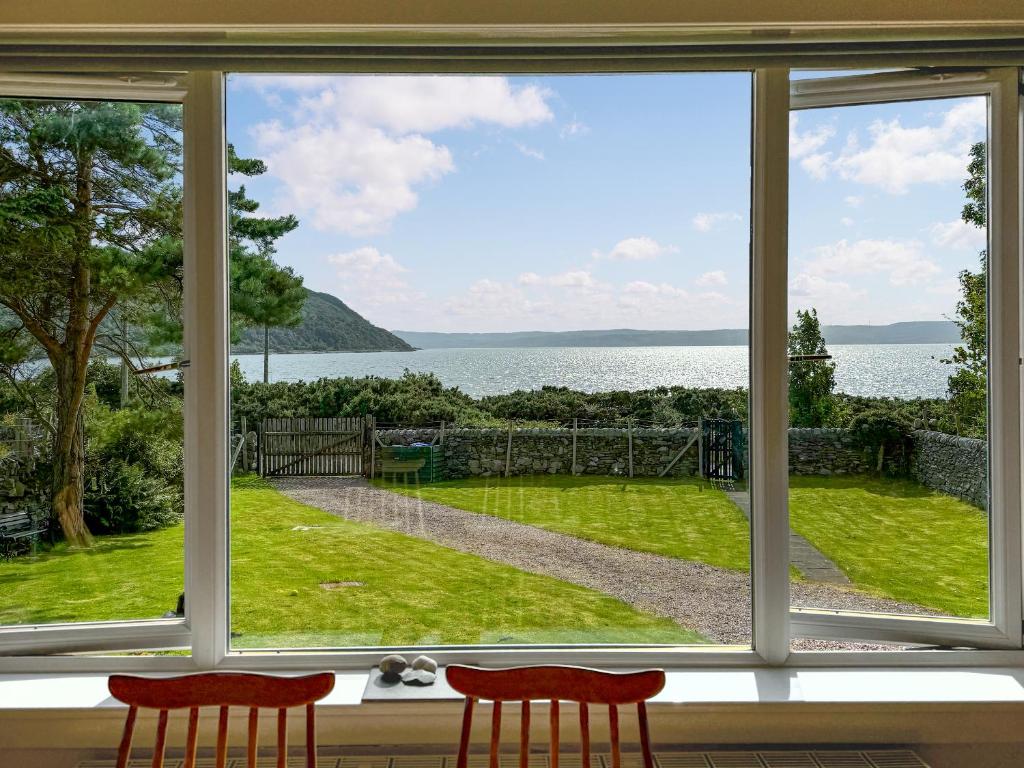a window with two red chairs looking out at the water at The Green in Lochranza