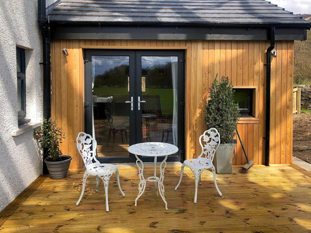 a patio with three chairs and a table on a deck at Clarinnes Cottage in Rowardennan