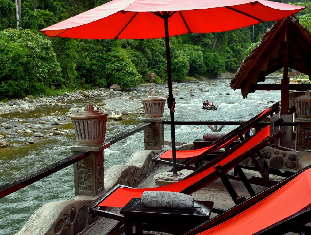 a boat with an umbrella and chairs and a river at EcoTravel Cottages Bukit Lawang in Bukit Lawang