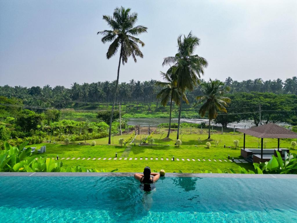 a woman in a swimming pool with a view of a resort at Pollachi Riverhouse, A CGH Earth Saha experience in Pollāchi