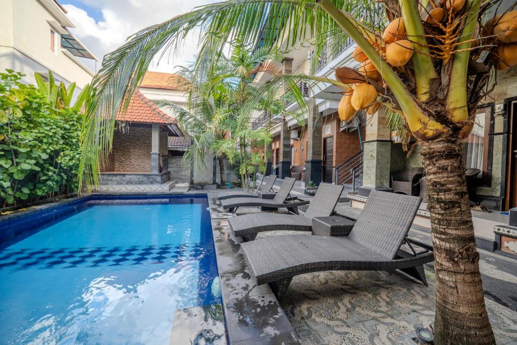 a resort pool with chairs and a palm tree at Wana Kubu Suite and Dormitory in Ngurah Rai International Airport
