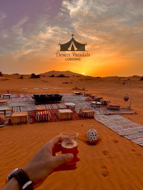a person holding a glass of beer in front of a desert paradise lodging at Desert Paradise Lodging in Merzouga