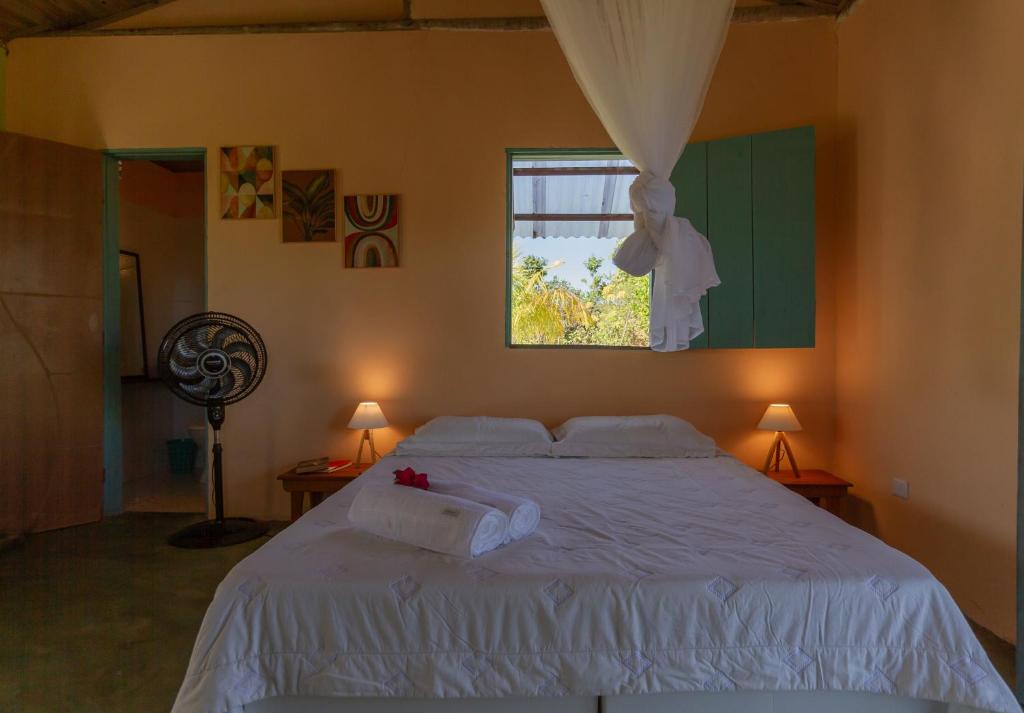 a bedroom with a white bed with a window at Chalé Pé de Araçá - Massarandupió in Entre Rios