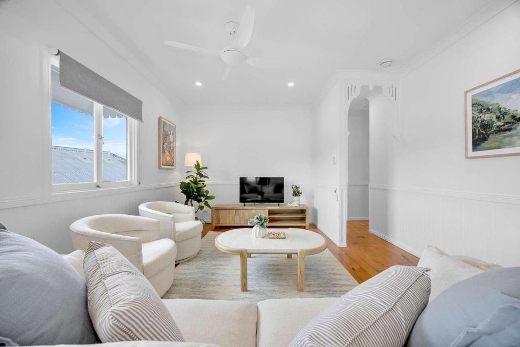 a white living room with a white couch and a table at 4 Bed Queenslander City Views Walk to Suncorp Deck + Parking in Brisbane