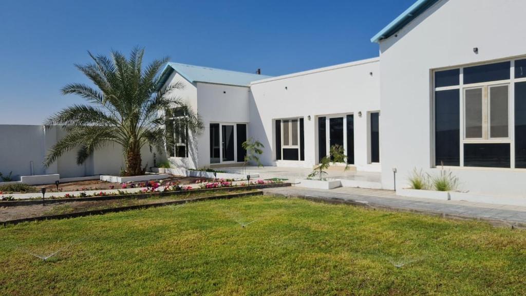 a white house with a palm tree and a yard at Riva chalet in Badīyah