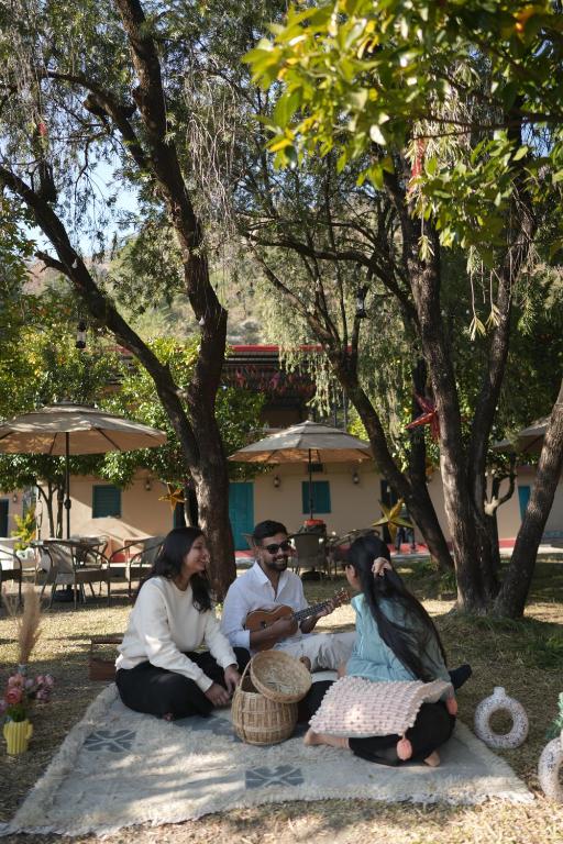 three people sitting on a blanket under a tree at NAMOH e VIRAASAT in Chopta