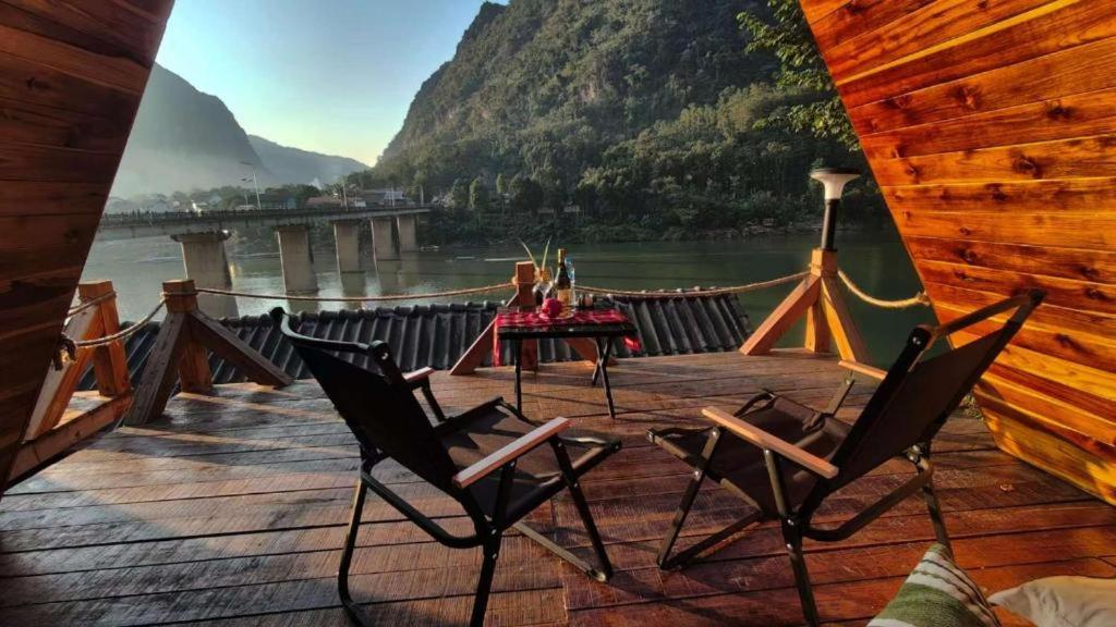 a wooden deck with chairs and a table on the water at Pont NongKhiaw in Nongkhiaw