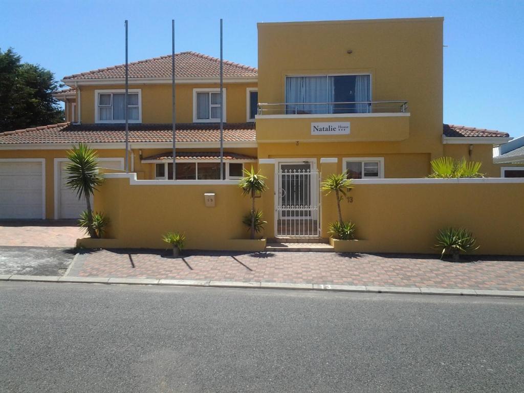 a yellow house with palm trees in front of it at Natalie Guesthouse in Bloubergstrand