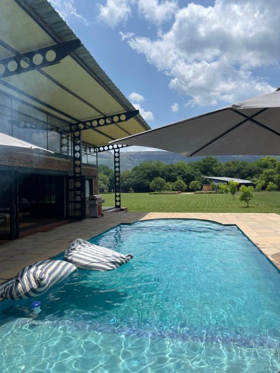 a swimming pool with an umbrella on a patio at Hartbeespoort Escape Hot Tub and Mountain Views in Skeerpoort