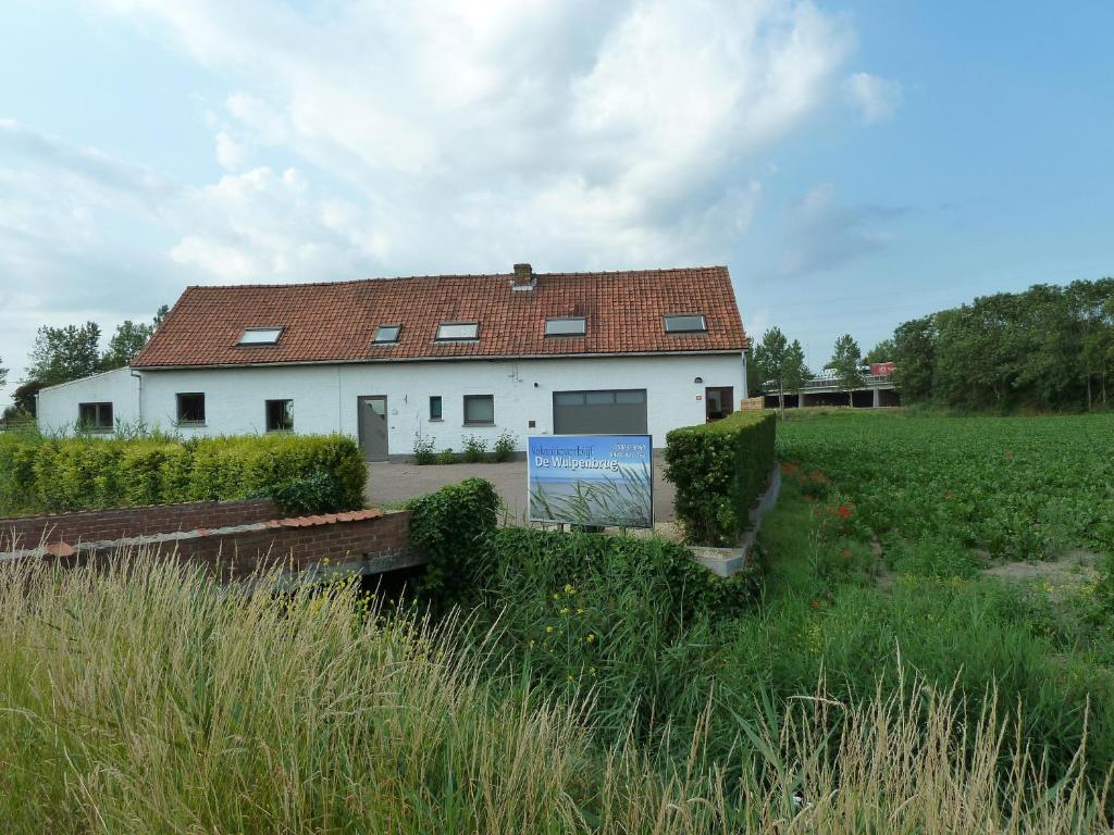 un bâtiment blanc avec un toit rouge dans un champ dans l'établissement Vakantiehuis 'De Wulpenbrug', à Wulpen