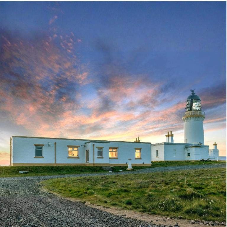 a white house with a lighthouse on a field at Self-catering Lighthouse Keeper's Cottage on the NC500 in Wick