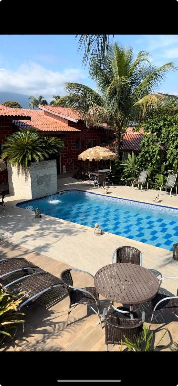 a swimming pool with chairs and a table next to a house at Ganesh Chalés in Boracéia