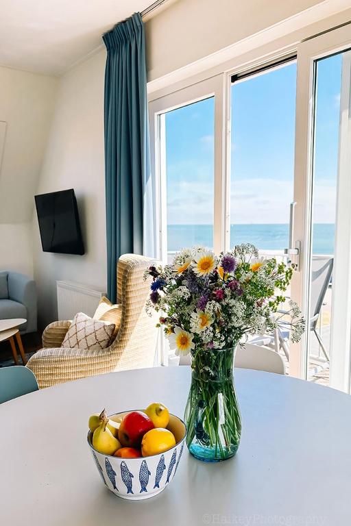 a vase of flowers and a bowl of fruit on a table at Appartement met uitzicht over de Wadden Zee in Oost-Vlieland