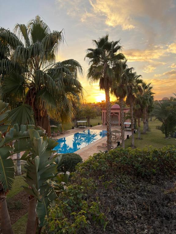 a pool with palm trees and a sunset in the background at Royal Moroccan House in Marrakesh