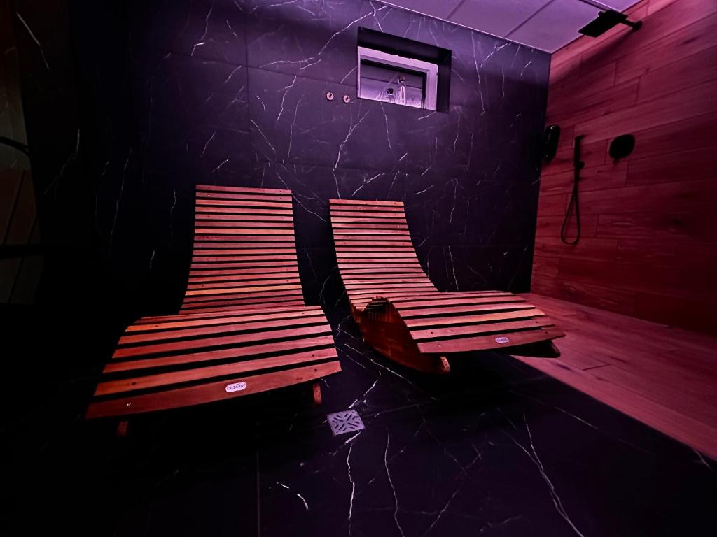 Dim spa lounge with two curved wooden chaise lounges, black marble floor and purple ambient lighting.