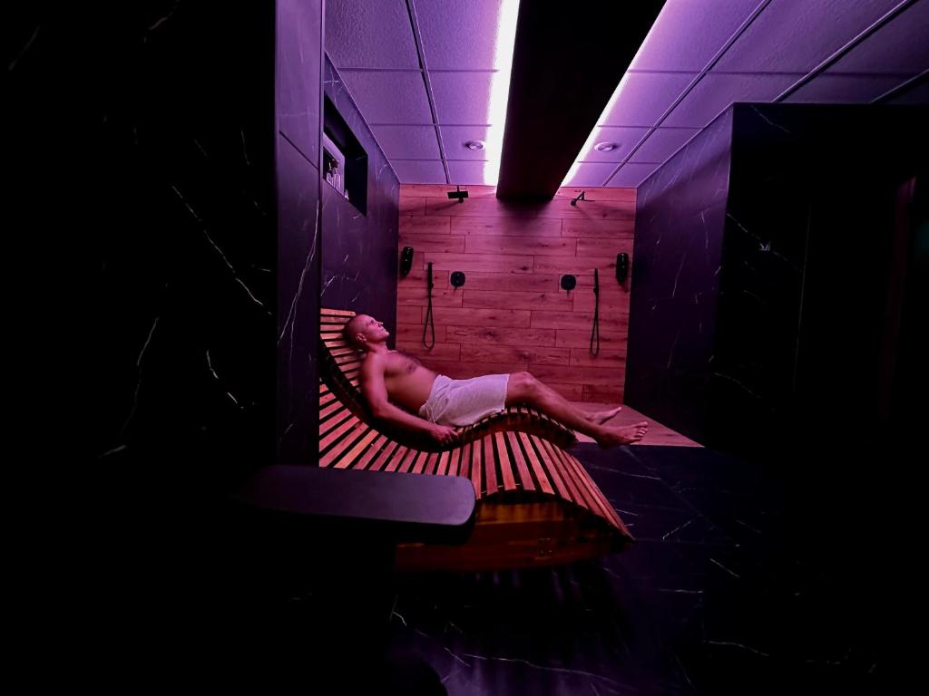 Man wrapped in towel reclining on wooden lounger in dimly lit spa relaxation room.