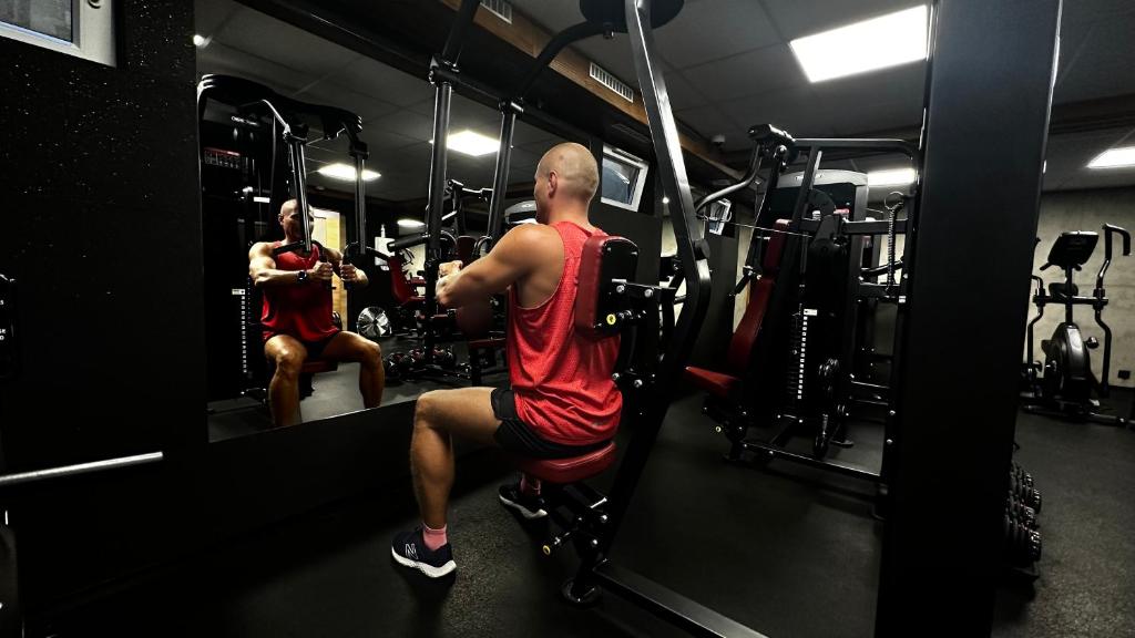 Person seated using chest fly machine, facing mirror in dimly lit gym.