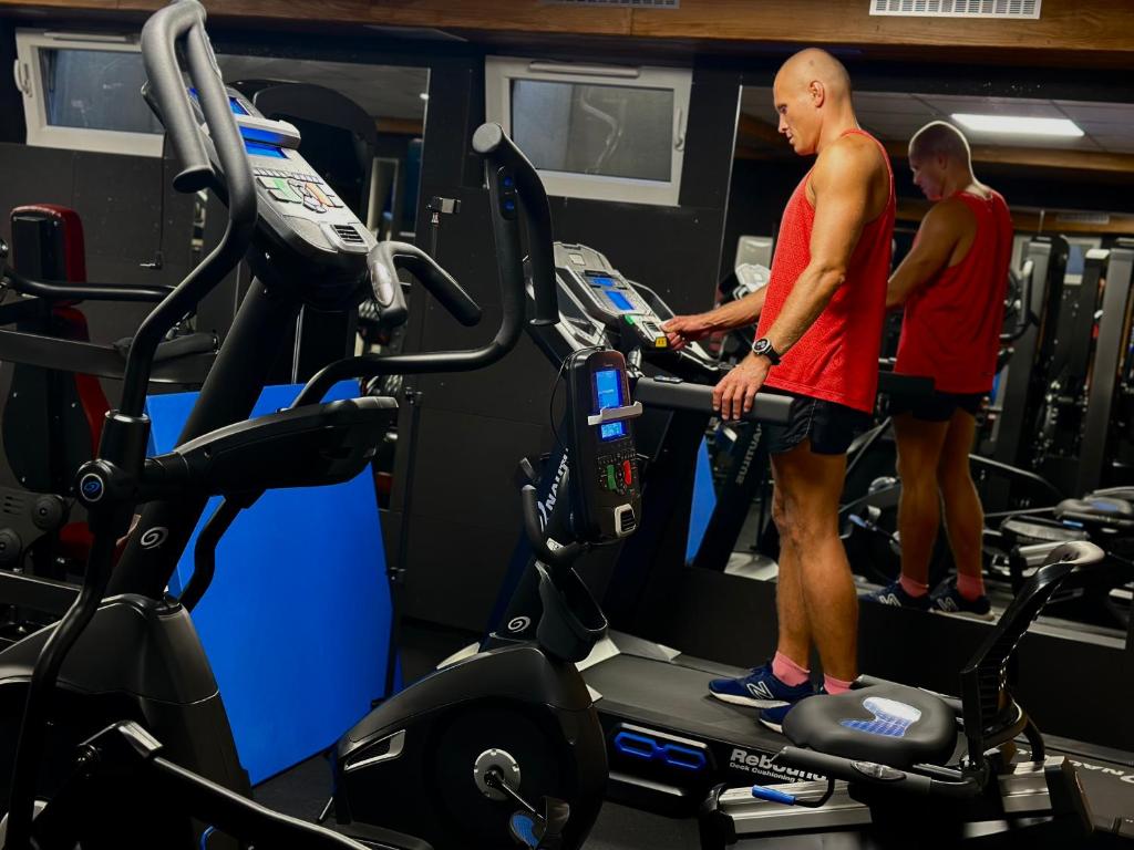 Person in red shirt standing on treadmill adjusting console, gym reflection visible.
