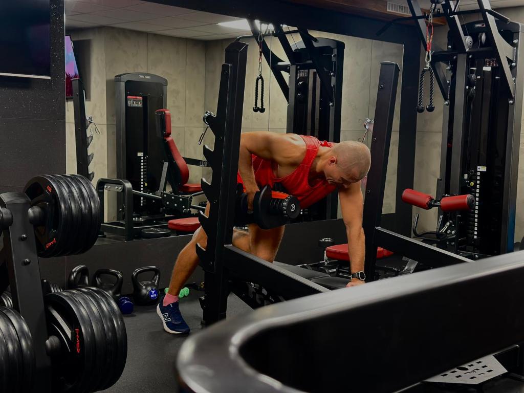 Person in red tank top doing a one-arm dumbbell row inside a mirrored home gym.