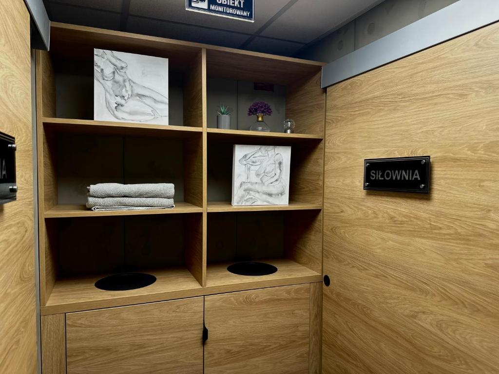 Wooden cubby shelving with folded towels, small plants, and framed sketches beside 'SIŁOWNIA' sign.
