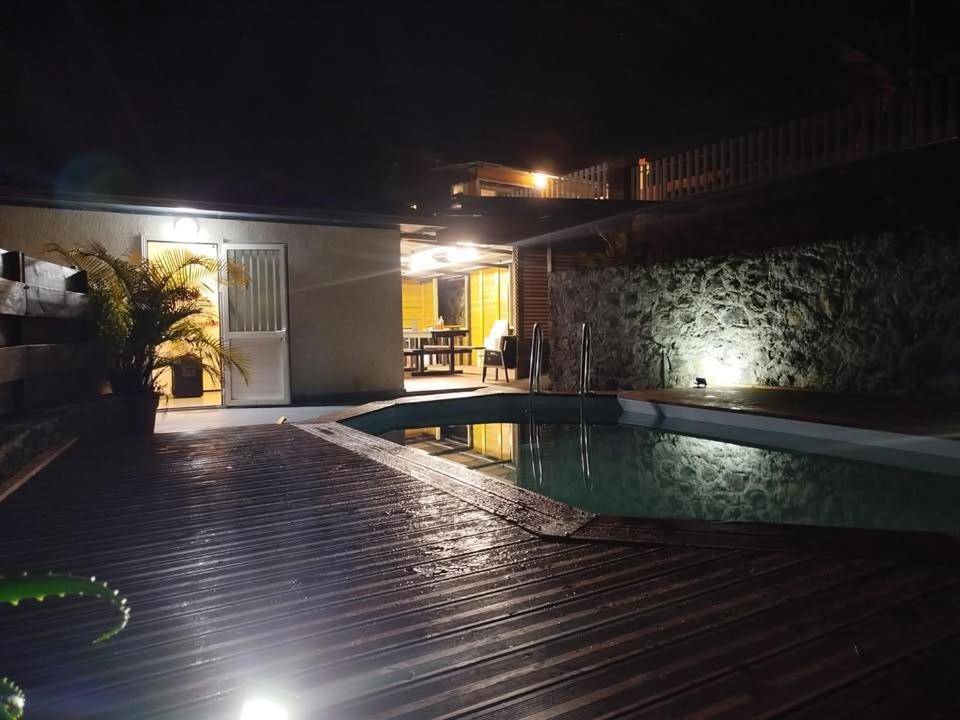 a swimming pool at night next to a house at Location Saisonnière Les Caféiers in Le Tampon