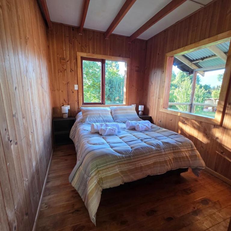 a large bed in a wooden room with two windows at Cabaña 2 - Rancho Doble AA in La Junta