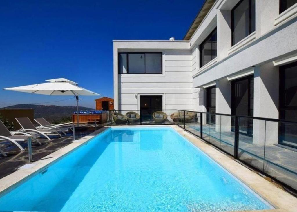 a swimming pool with chairs and an umbrella next to a house at ממלכת החלומות - וילה מהממת עם בריכה פרטית מחוממת מקורה ונוף מהמם in ‘Ein el Asad