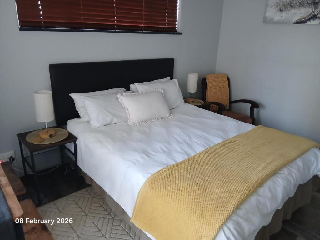 a bedroom with a large white bed with a side table at Aroha Guest Apartment in Roodepoort