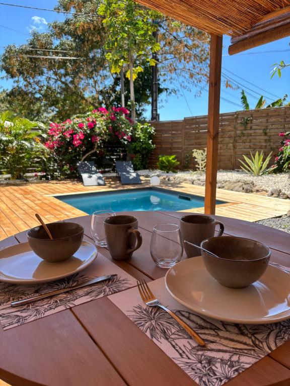a table with bowls and glasses on a table in front of a pool at Le Frangipanier Cozy Bungalow in Le Moule