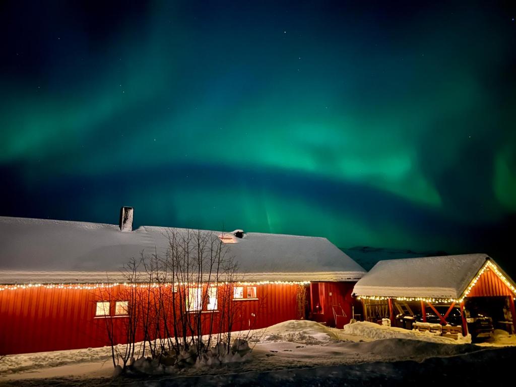 an aurora over a red barn in the snow at Aurora beach house in Trondalen