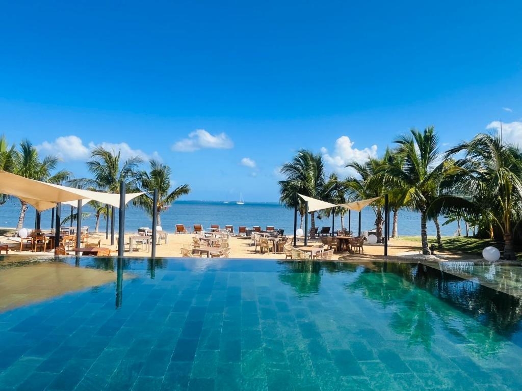 a swimming pool next to a beach with palm trees at Beachfront sea view apartment in Petite Case Noyale