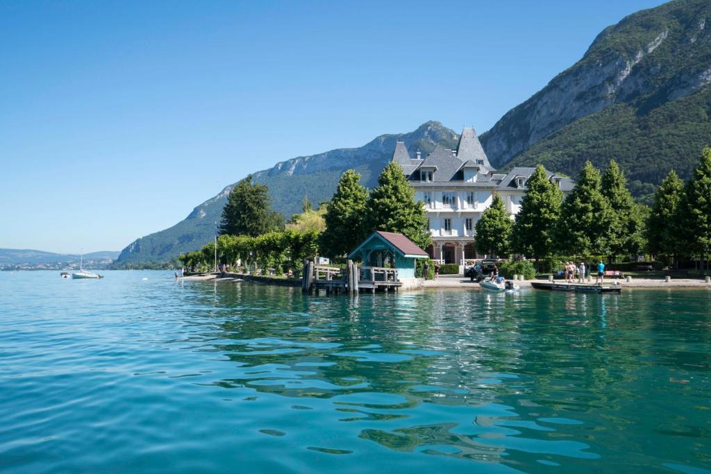 un gran edificio a orillas de un cuerpo de agua en Le Pavillon des Fleurs en Menthon-Saint-Bernard