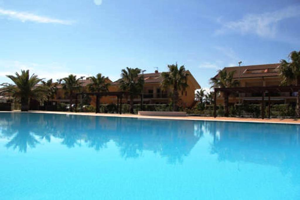 a large blue swimming pool with palm trees and buildings at Residence Dei Margi in Torre Faro