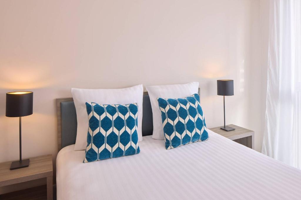 a bedroom with a bed with blue and white pillows at Quality Aparthotel Morangis Orly in Morangis
