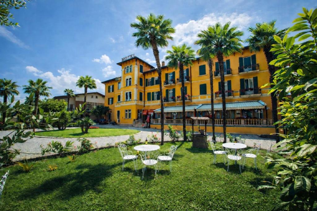 a large yellow building with tables and palm trees at Hotel Maderno by Double Hospitality in Toscolano Maderno