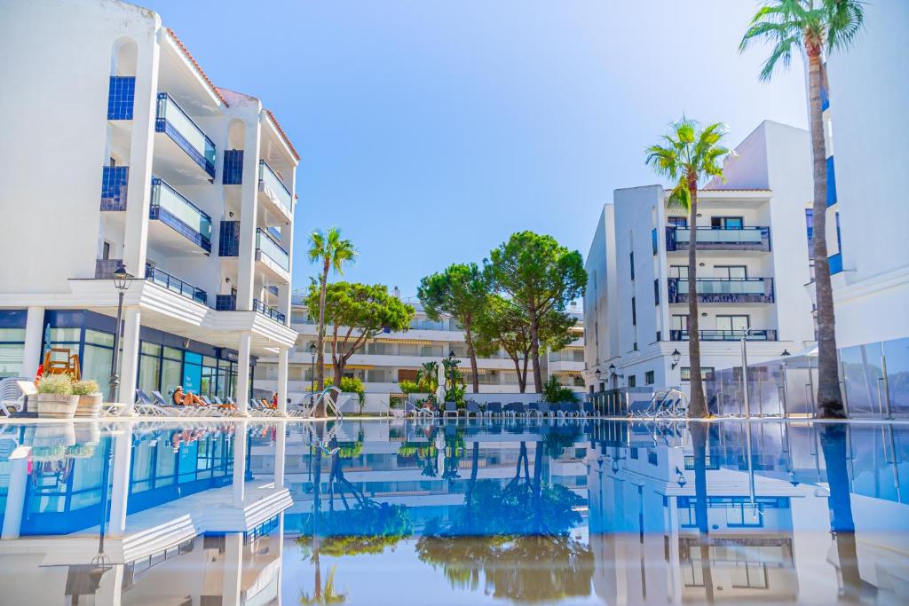 a swimming pool in front of a building with palm trees at Pins Platja Apartments in Cambrils