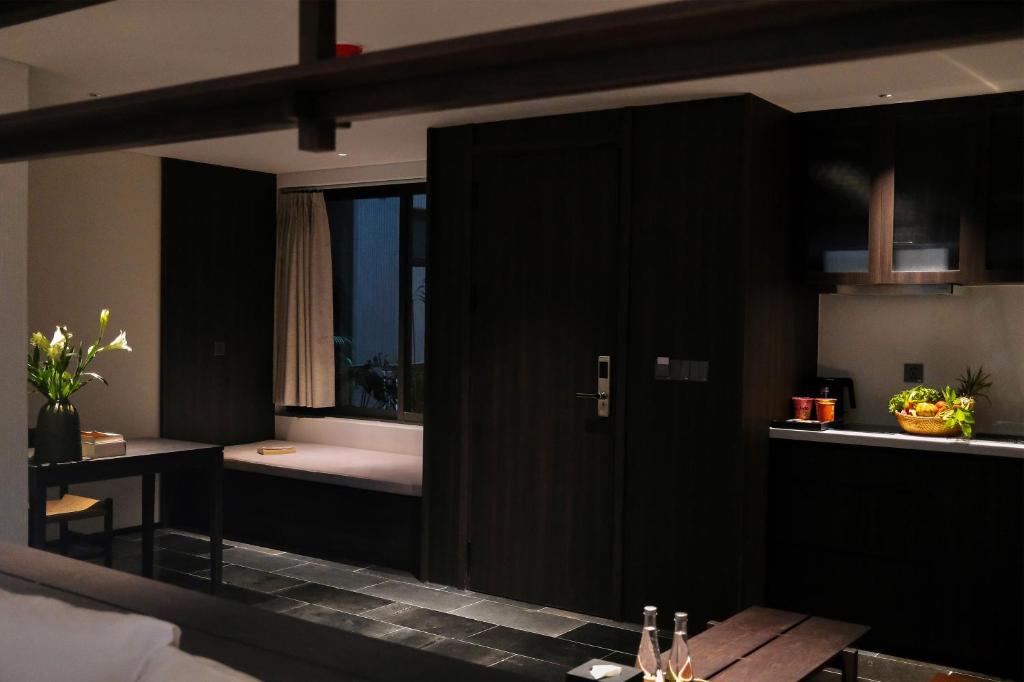 A dark wood apartment interior showing the bedroom edge, bathroom door and kitchenette.