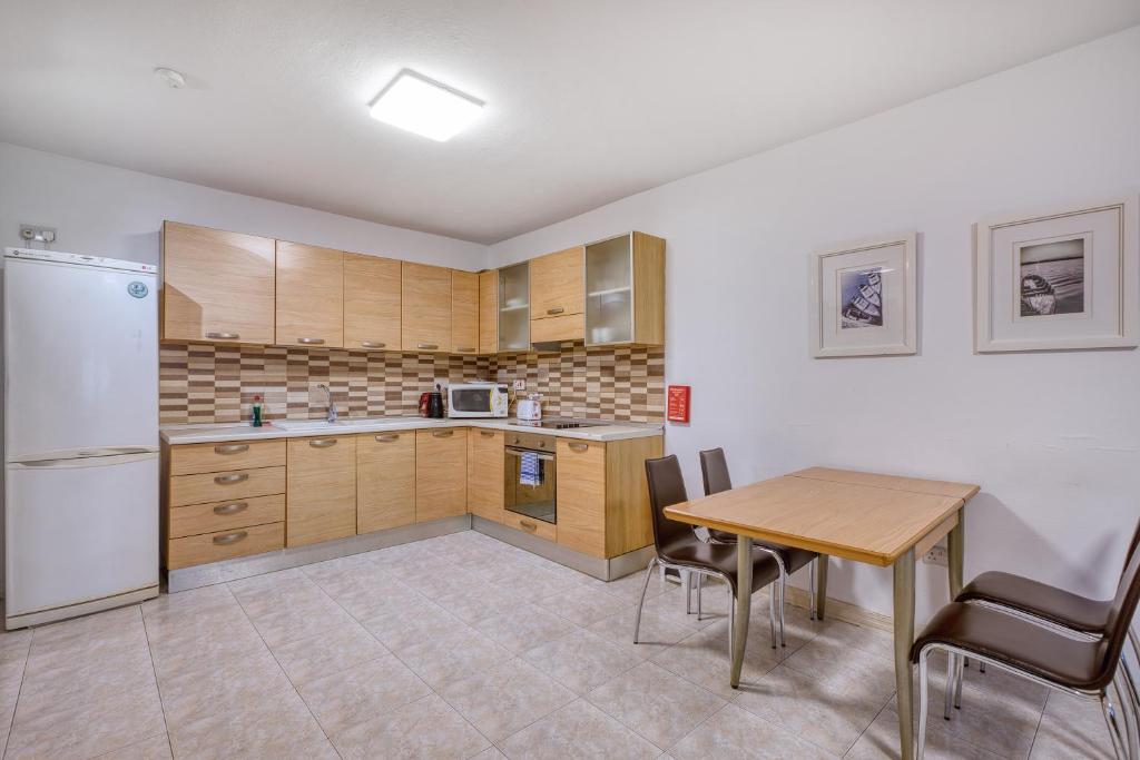 a kitchen with wooden cabinets and a table and a refrigerator at Budget Friendly apartment in Central Swieqi - 10 minutes walk to Paceville & the beach in St. Julianʼs