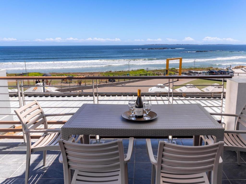 a table with a bottle of wine on top of a balcony with the beach at 167 Eden on the Bay in Big Bay