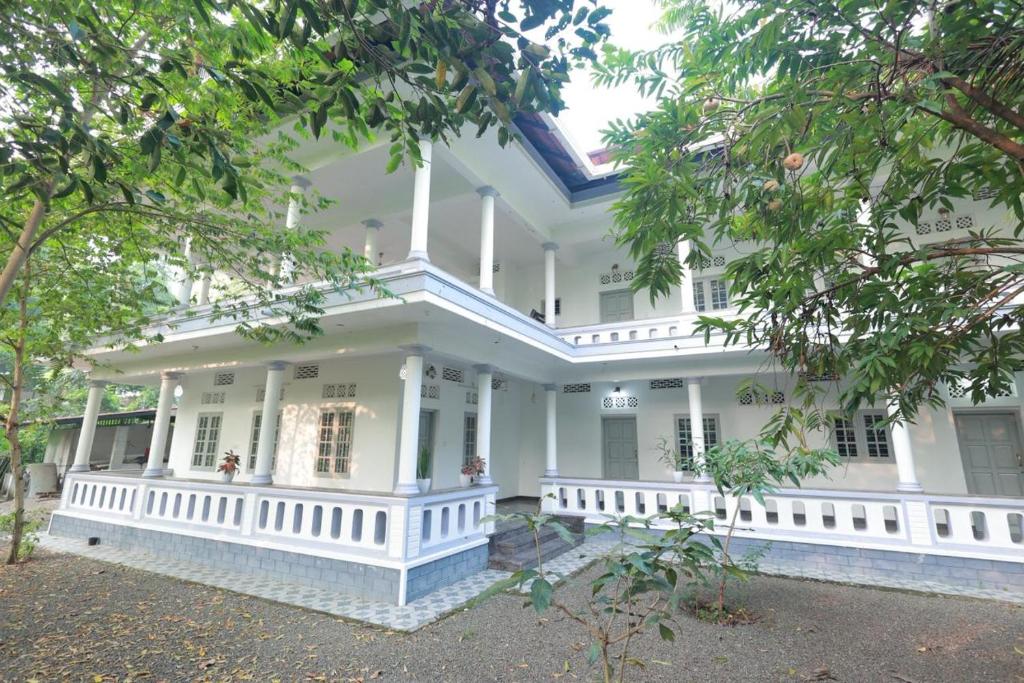 a white house with a porch and trees at Greenhaven Homestay Villa in Ettumānūr