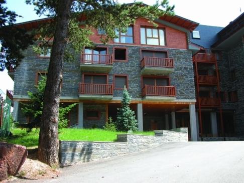 un gran edificio de ladrillo con un árbol delante de él en Apartamentos Solineu, en La Molina