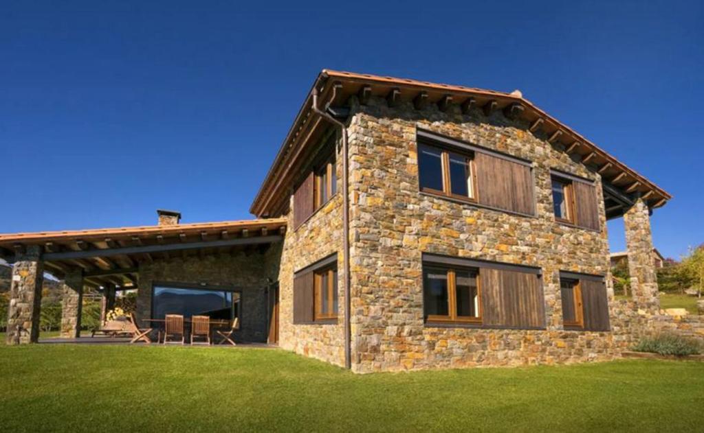 ein großes Steinhaus mit einem Holzdach und grünem Gras in der Unterkunft CasaCampelles II - Vall de Núria - Ripollès in Campelles