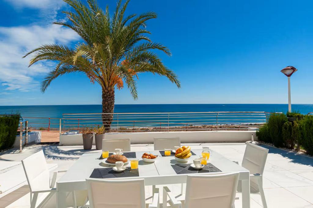 a table and chairs on a patio with a palm tree and the ocean at Infinity View apartment in Arenales del Sol