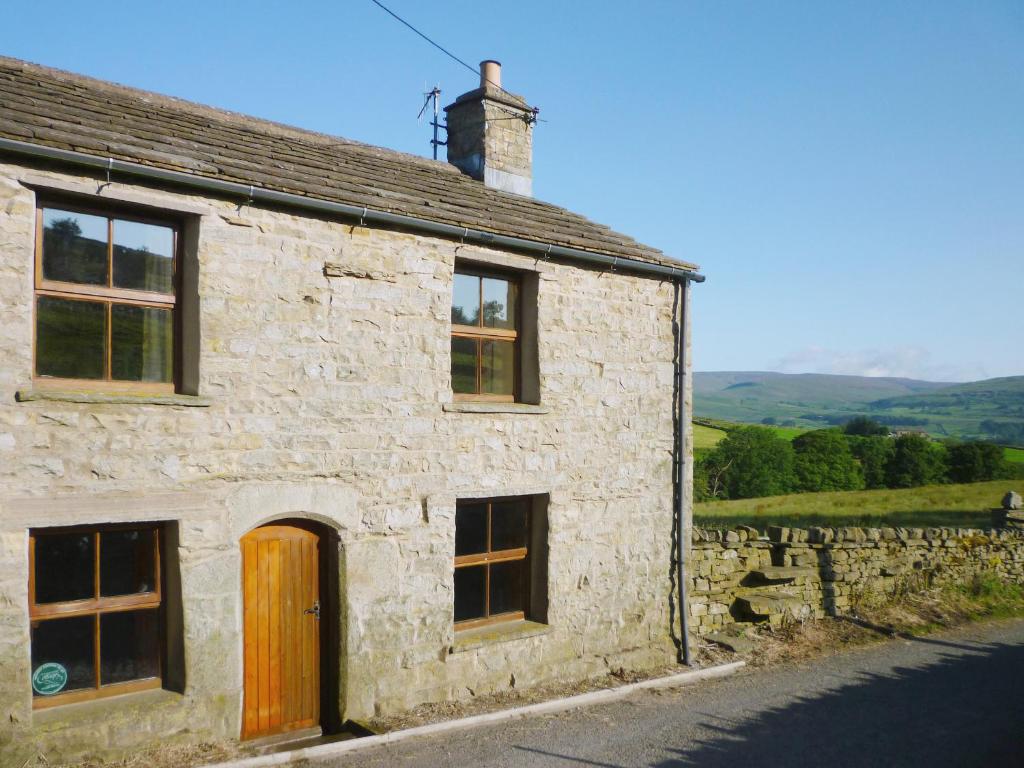 a stone house with a wooden door on a street at Aysgill Cottage in Hawes